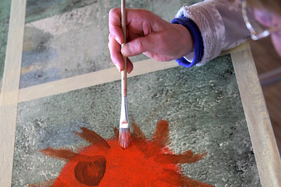 Das Bild zeigt eine Hand die einen Pinsel über ein Gemälde führt.