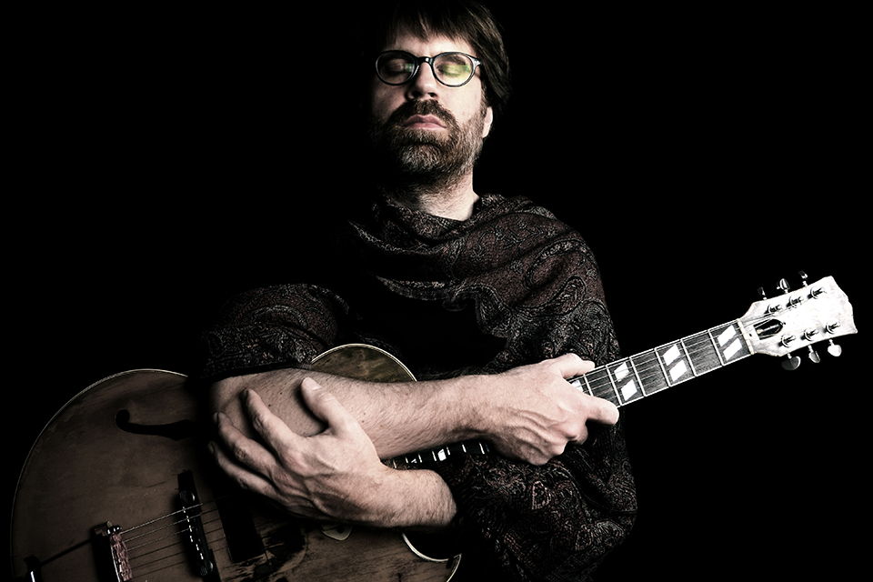 Das Bild zeigt ein Porträt von Hub Hildenbrand mit seiner Gitarre.