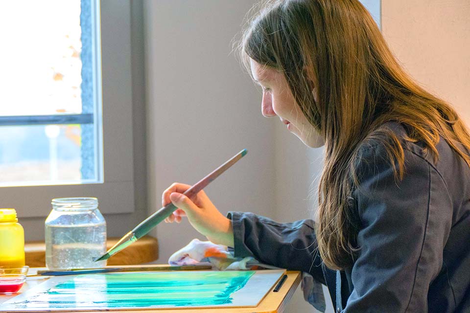 Das Bild zeigt ein Mädchen beim Malen mit Wasserfarbe.